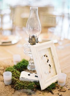 an old photo frame sitting on top of a moss covered table next to candles and glasses