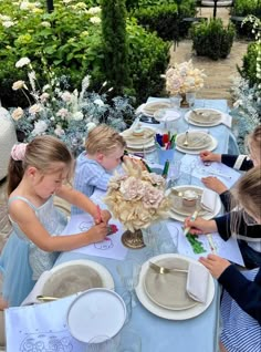 several children sitting at a table with plates and flowers