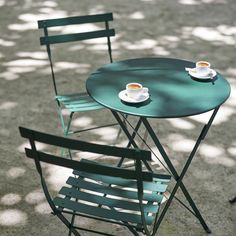 two chairs and a table with cups of coffee sitting on them in the middle of a park