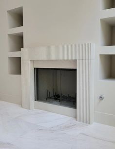 an empty room with a white fireplace and shelves on the wall, in front of it