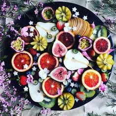 a plate filled with cut up fruit on top of a table next to purple flowers