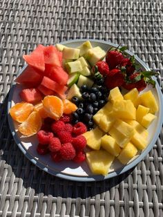 a white plate topped with fruit on top of a wicker tablecloth next to watermelon, raspberries, oranges and strawberries