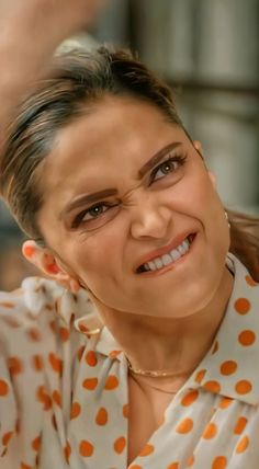 a woman is smiling as she combs her hair with an orange polka dot shirt