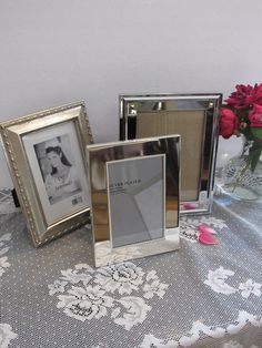 three silver frames sitting on top of a table next to a vase filled with flowers