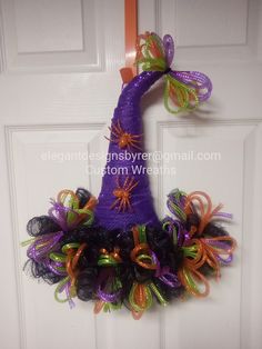 a purple witch's hat wreath hanging on a door with orange and green streamers