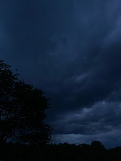 dark clouds loom in the sky over a field at night with a lone tree