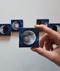 a person holding up four small square coasters with the moon on them in front of three smaller ones