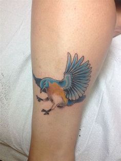 a bird tattoo on the leg of a woman's leg, with an orange and blue wing