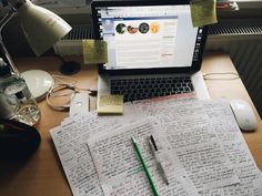 an open laptop computer sitting on top of a wooden desk covered in notes and papers