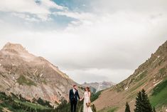 a bride and groom holding hands in the mountains