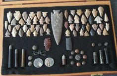 an assortment of ancient artifacts is displayed in a wooden case on a black cloth covered table