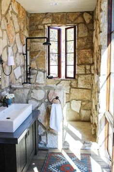 a bathroom with stone walls and flooring, including a sink in the corner next to a window