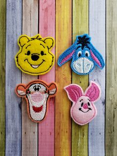 three winnie the pooh and piglet appliques hanging on a wooden fence