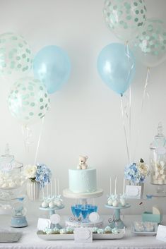 a table topped with lots of blue and white balloons next to a cake covered in confetti