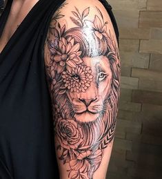 a woman with a lion and flowers tattoo on her arm is standing in front of a brick wall