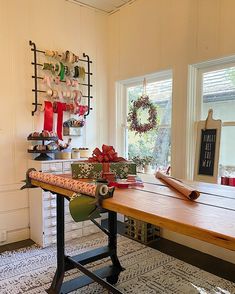 a wooden table topped with lots of christmas presents next to a wall mounted shelf filled with wreaths