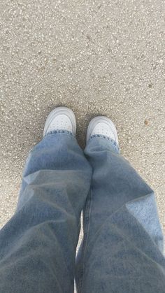 the bottom view of someone's feet in jeans and white tennis shoes on concrete