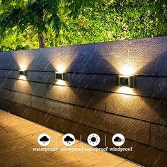 four lights on the side of a wall with trees in the background and rain coming down