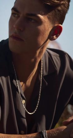 a young man wearing a black shirt and silver necklace