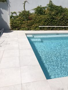 an empty swimming pool in the middle of a patio with chairs and bushes behind it