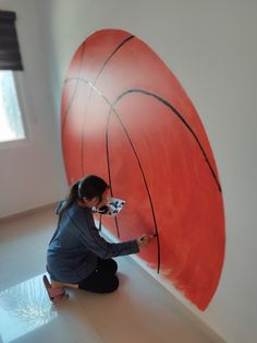 a woman sitting on the floor painting a basketball