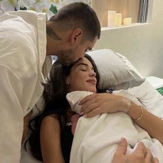 a man and woman cuddle in bed with the baby wrapped in a white blanket