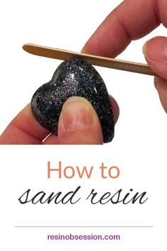 a hand holding a small black rock with the words how to sand resin on it