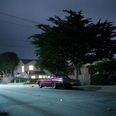 a purple car parked on the street in front of a house at night with its lights on