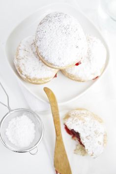 three powdered sugar covered pastries on a white plate with a wooden spoon and measuring cup