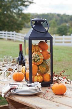 a lantern with pumpkins and gourds is sitting on a wooden table outside