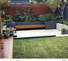 an outdoor garden with plants and benches in the grass, next to a wooden fence