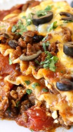 a white plate topped with lasagna covered in meat and olives on top of it