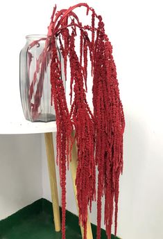 a glass vase filled with red yarn next to two wooden sticks and a green table