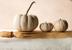 three white pumpkins sitting on top of a piece of wood next to each other