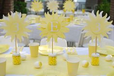 the table is set up with yellow and white paper sunflower centerpieces, cups, and napkins