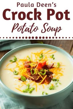 a bowl of potato soup with bacon, cheese and green onions in it on a wooden table