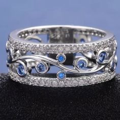 a white gold ring with blue sapphires and diamonds on the sides, sitting on top of a black cloth