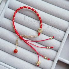 a red string bracelet with gold charms and beads on it, sitting in a box