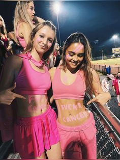 two young women in pink outfits standing next to each other at a baseball game with their arms around one another