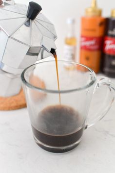 coffee being poured into a glass cup with an umbrella shaped teapot in the background