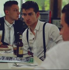 three men sitting at a table with food and drinks