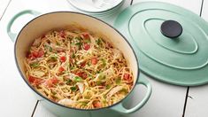 a pot filled with pasta and vegetables on top of a wooden table next to plates