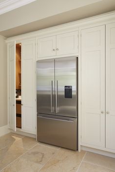 a stainless steel refrigerator in a kitchen with white cabinets and marble flooring on the walls