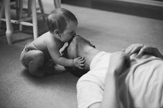 a black and white photo of a baby playing with his dad's leg on the floor