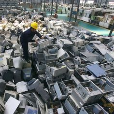 a man standing on top of a pile of old computer equipment in a factory filled with lots of monitors