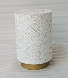 a white vase sitting on top of a table next to a white sheet covered wall