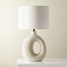 a white lamp sitting on top of a table next to a white dresser and wall