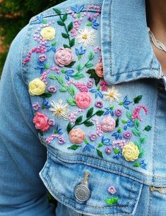 a woman wearing a jean jacket with flowers on it and a coin in her pocket