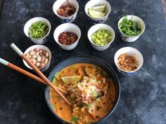 several bowls of food with chopsticks on the table next to them and various toppings