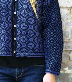 a woman standing in front of a brick wall wearing a blue and black cardigan